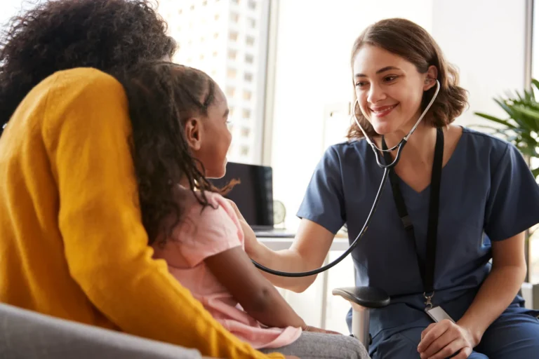 A nurse exemplifies patient-centered healthcare by using a stethoscope to gently examine a young girl sitting with an adult in a medical office.